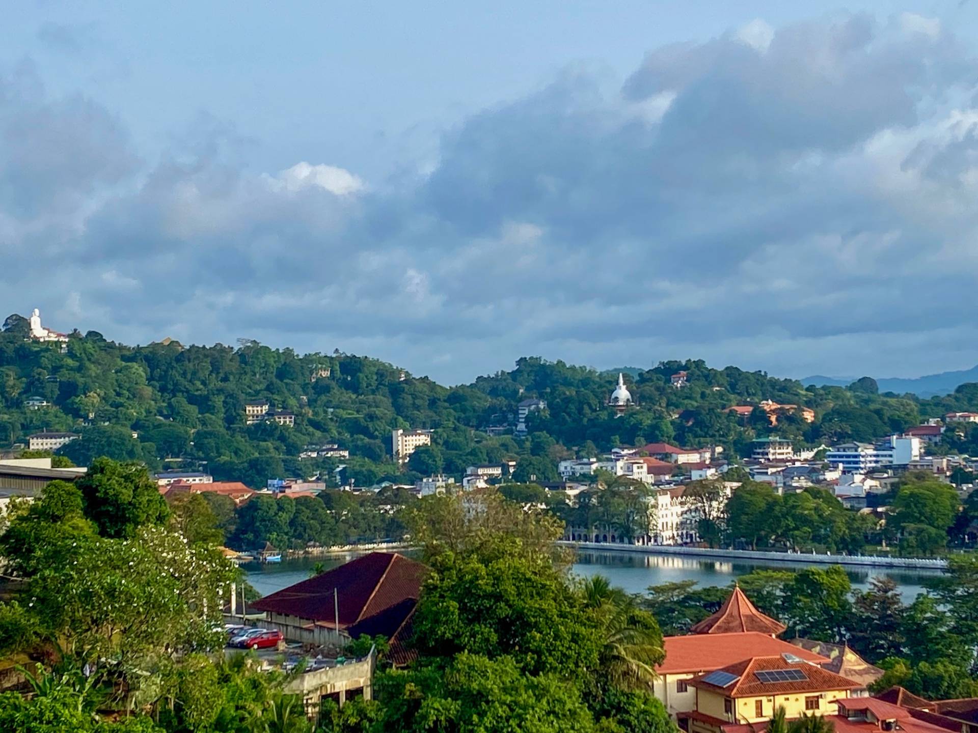 Kandy from a hillside: red roofs and trees around Kandy Lake, the Temple of the Tooth on the far shore and the white Buddha statue on the hill