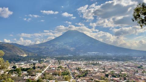 Antigua Guatemala's tiled roofs and grid of streets below the cone of Volcan de Agua under scattered clouds