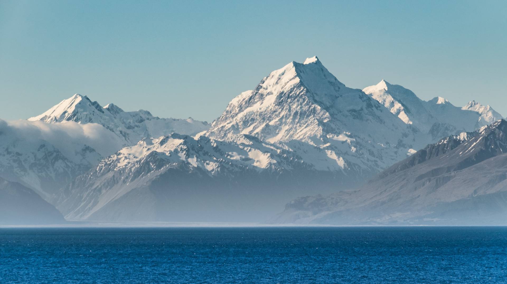 Snow-covered Aoraki/Mount Cook rising above a band of low cloud with the deep blue water of Lake Pukaki in the foreground