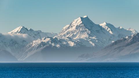 Snow-covered Aoraki/Mount Cook rising above a band of low cloud with the deep blue water of Lake Pukaki in the foreground