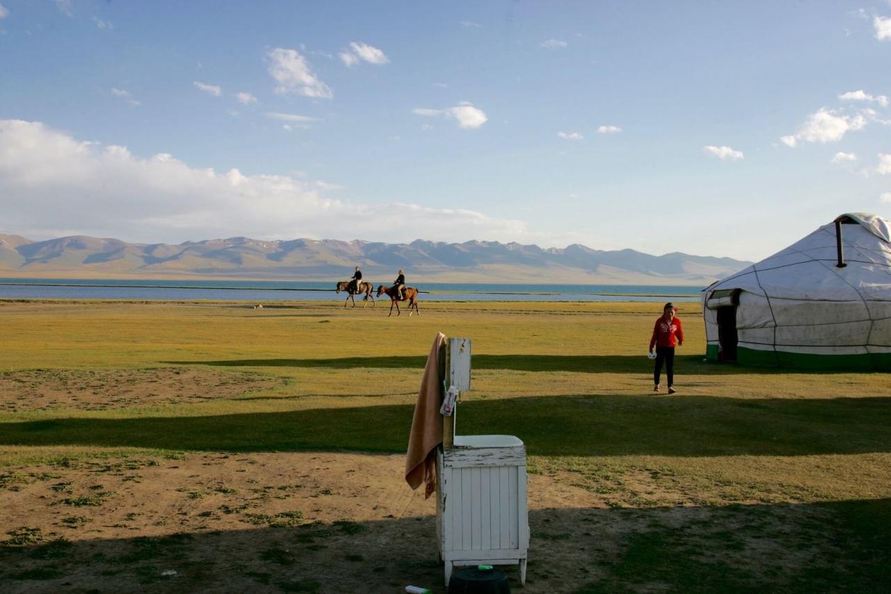 Yurts and riders beside Song-Kul lake with mountains across the water