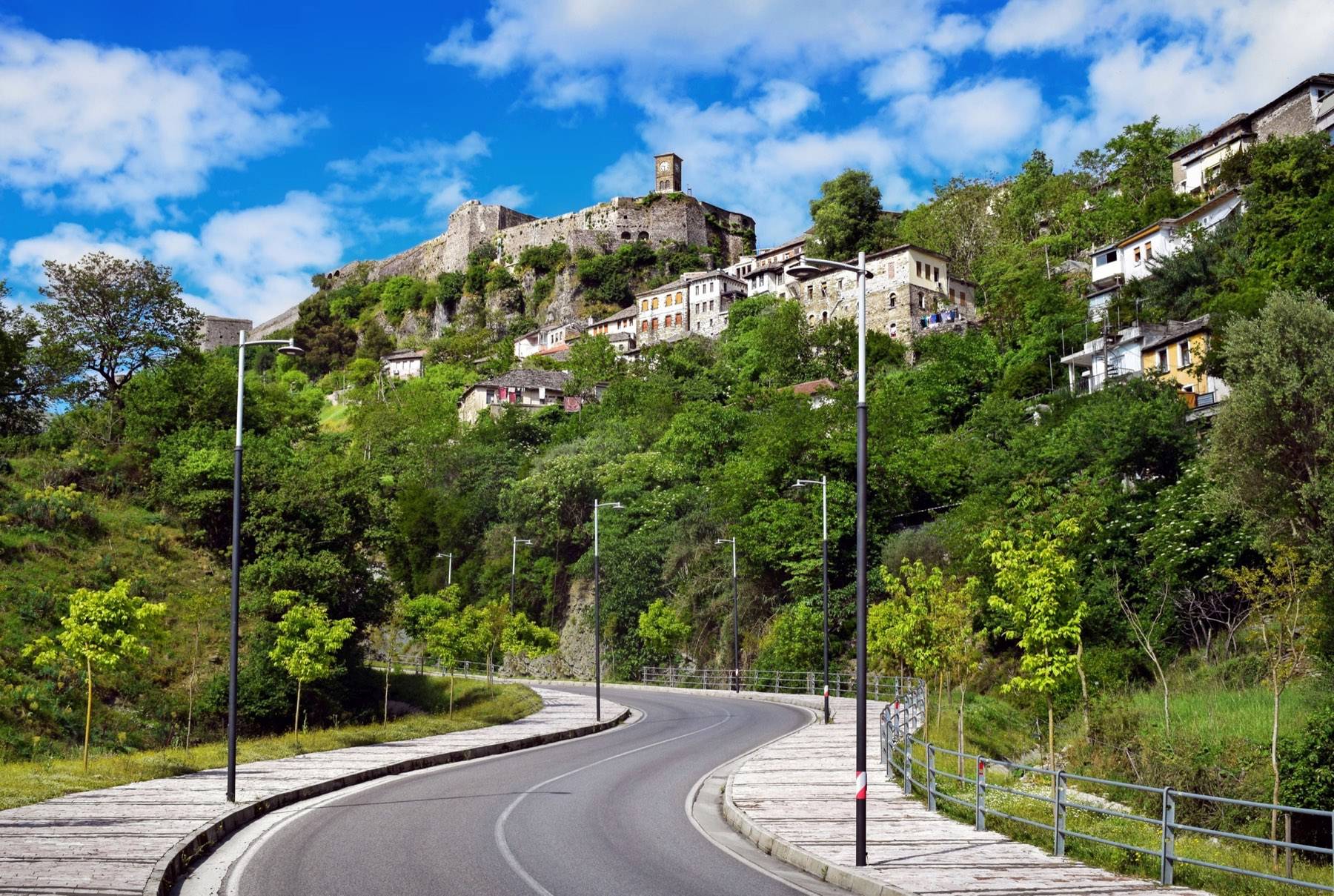 Gjirokaster Castle and clock tower above hillside houses and a curving road