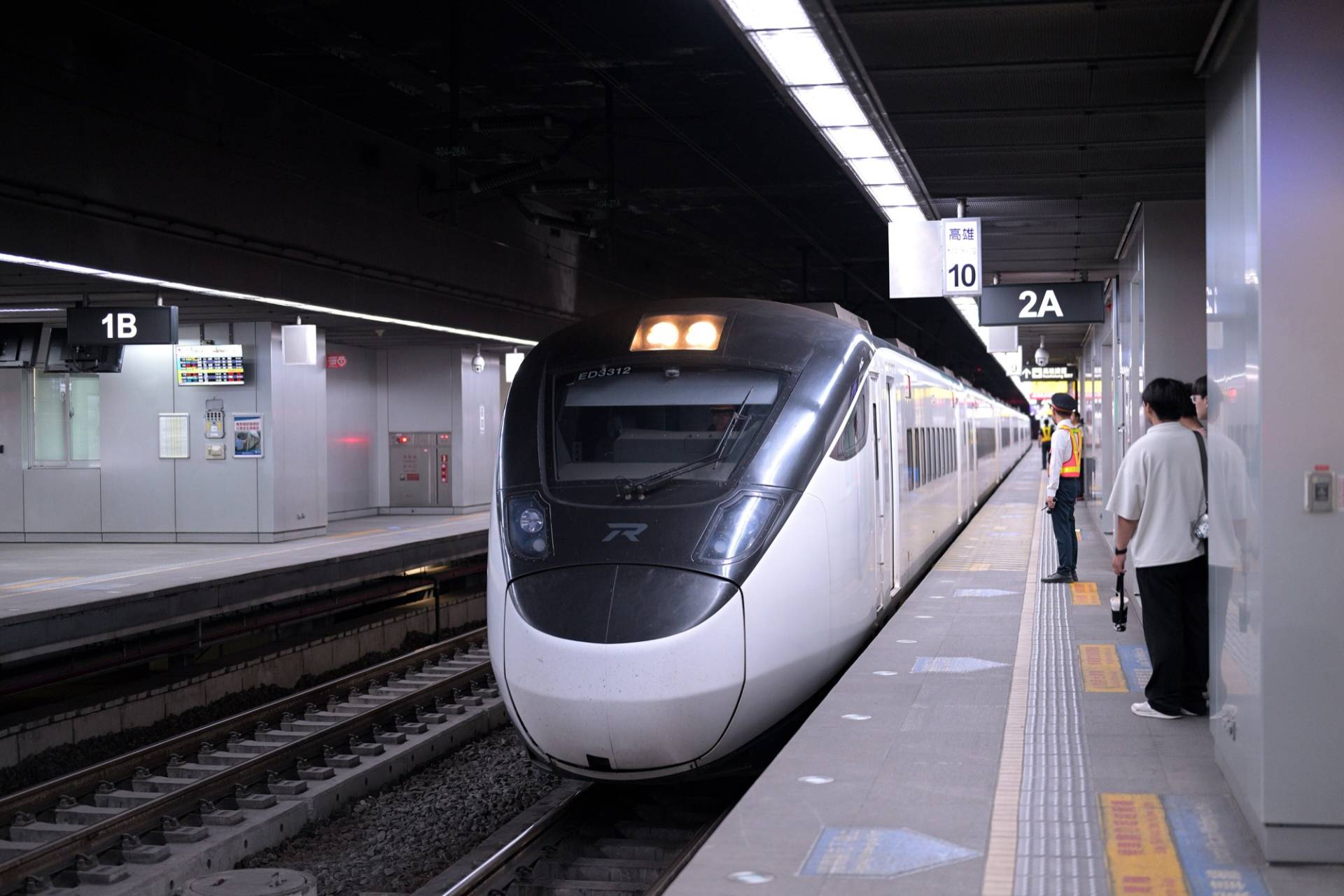 A white and black Taiwan Railway EMU3000 express train arriving at an underground platform at Kaohsiung station while passengers wait