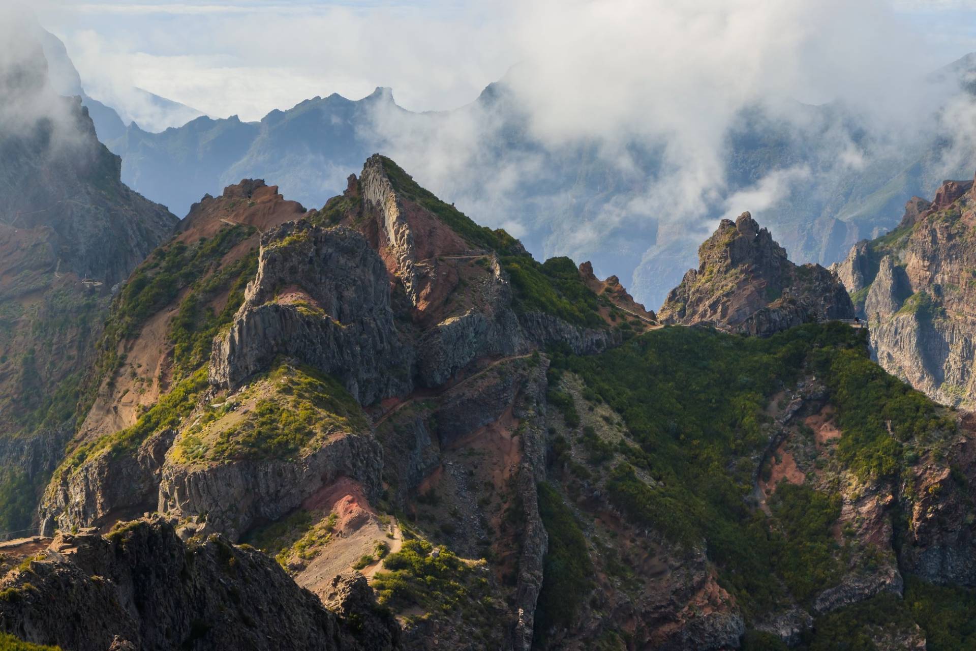 Jagged green and brown ridge near Pico do Arieiro with cloud banks drifting through the gaps between the peaks