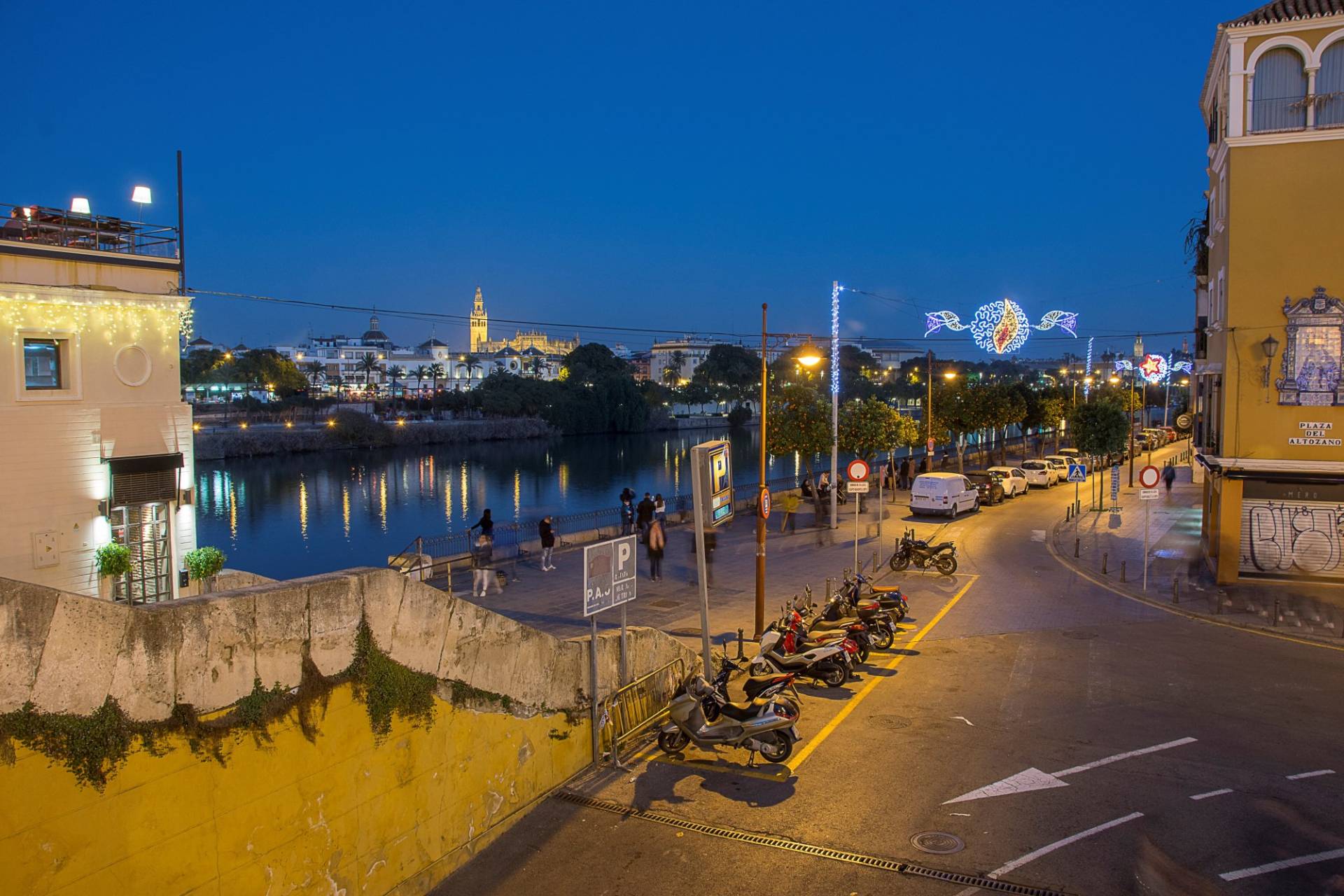 Seville at dusk from the Triana bank in early January: Christmas lights over the street, the Guadalquivir and the Giralda on the skyline