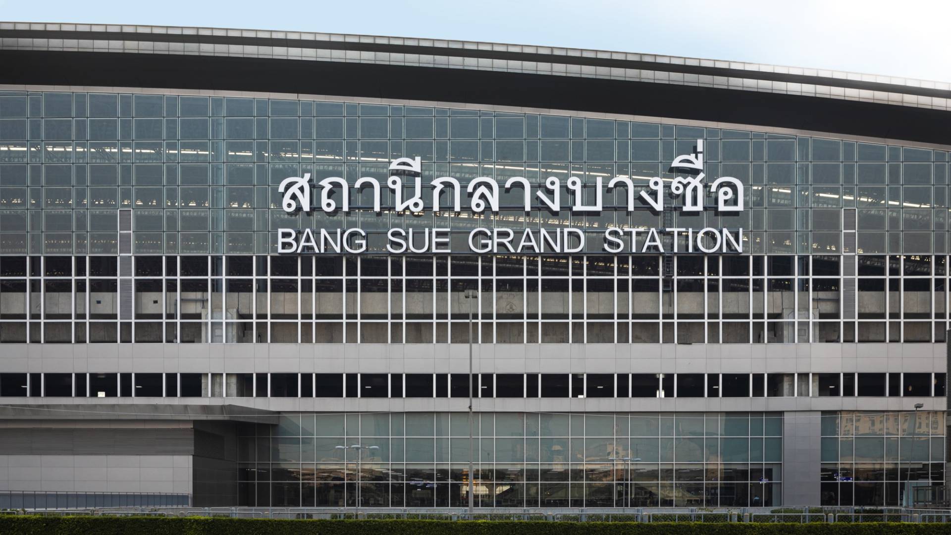 Glass-and-steel facade of Bangkok's central railway terminal with large Thai and English signage reading Bang Sue Grand Station, its name before it became Krung Thep Aphiwat Central Terminal