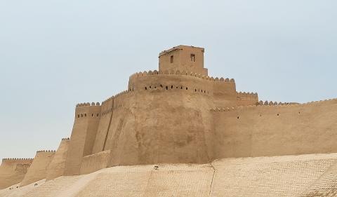 Earthen walls and a tower of Itchan Kala in Khiva beneath a pale sky