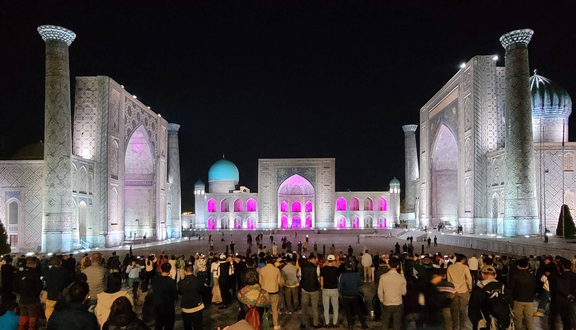 Three illuminated madrasas and visitors at Registan square in Samarkand at night