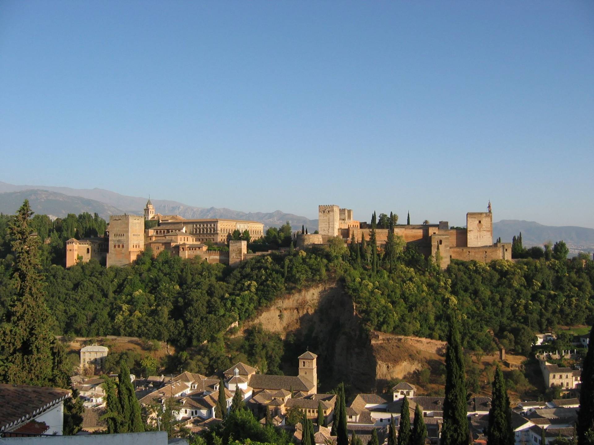 The Alhambra's towers and the Generalife on their wooded hill seen from the Albaicin, with the Sierra Nevada behind under a clear sky